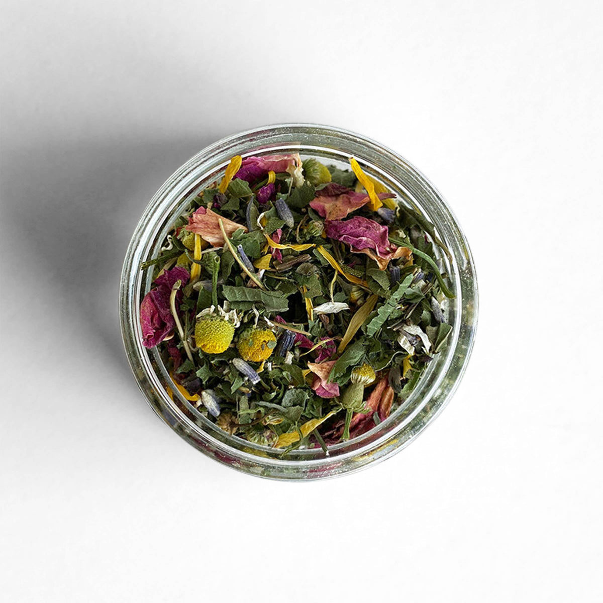 Top view of an open glass jar of Poet herbal tea, a blend of rose petals, chamomile, lavender, calendula and mint leaves