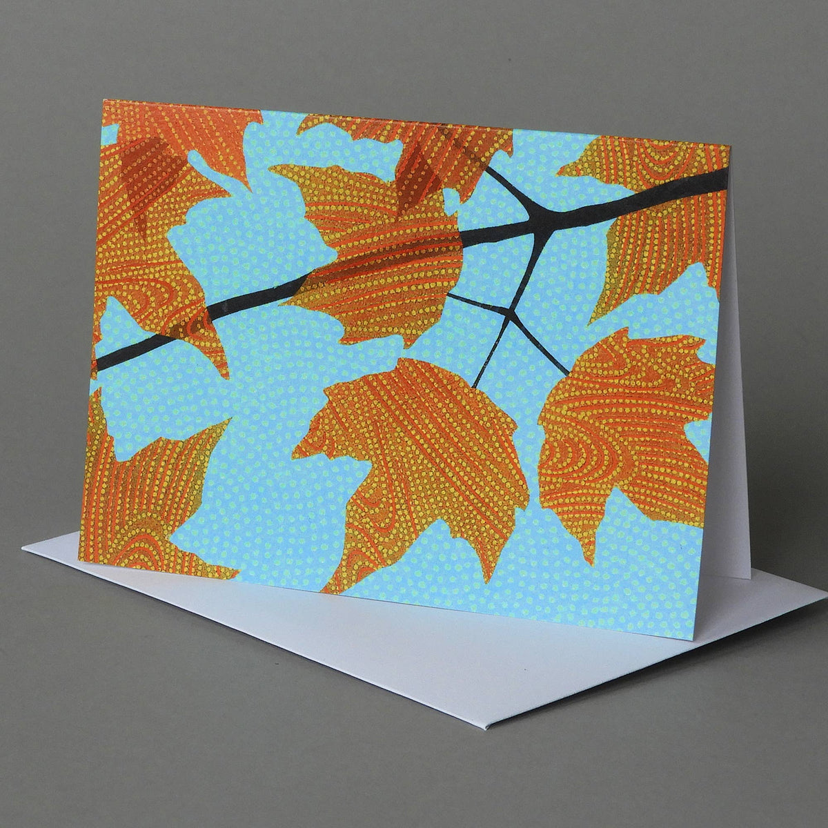 Autumn Canopy notecard of orange maple leaves and a dark branch against a bright blue sky, on an envelope