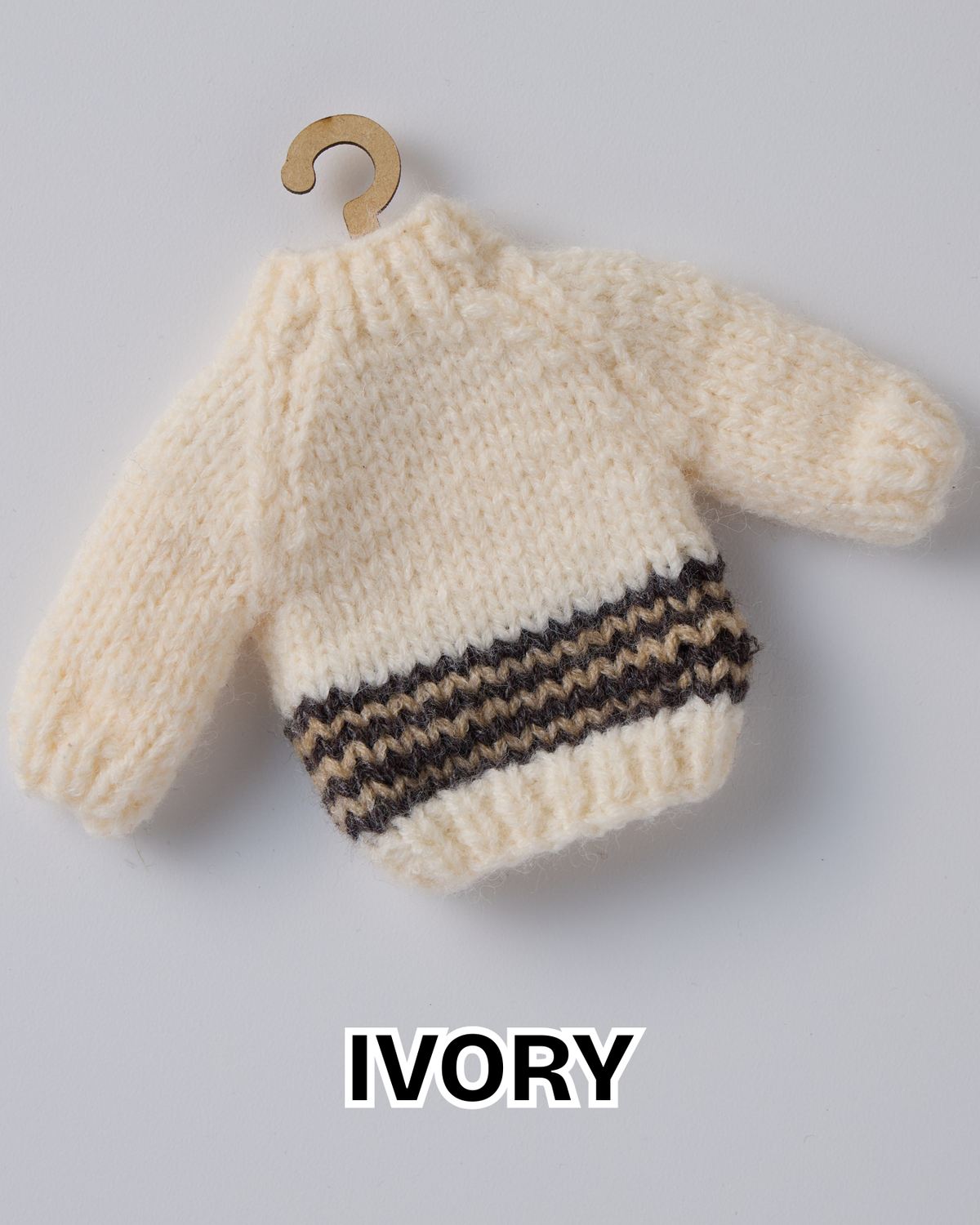 Ivory hand knit mini sweater ornament with a brown and tan striped hem on a wooden hanger
