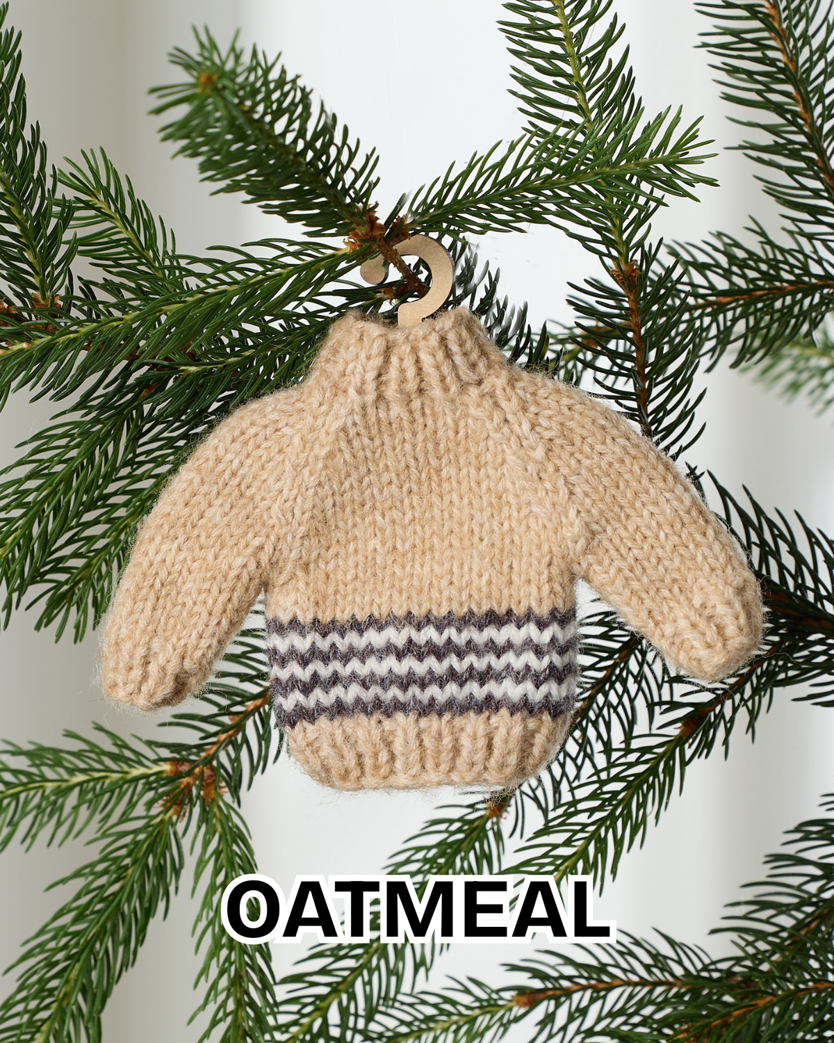 Oatmeal mini knit sweater ornament hanging on an evergreen branch