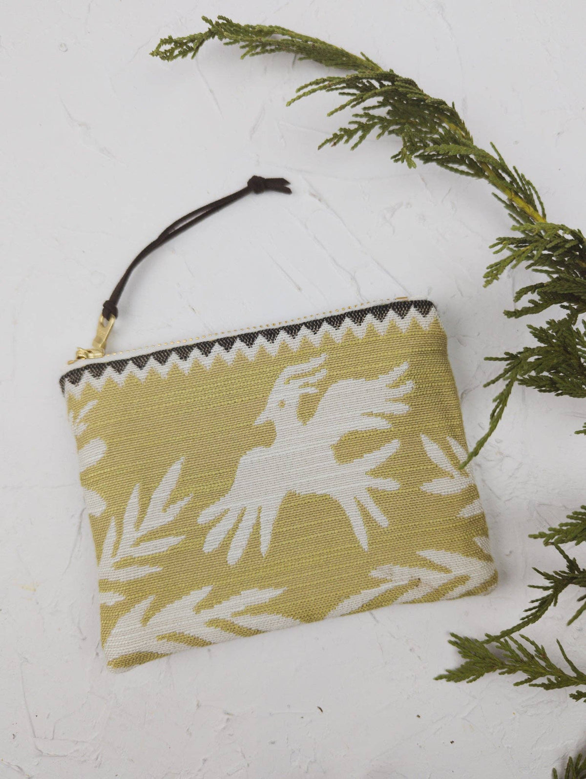 Folk Life mini pouch in olive green with a white bird silhouette and fern print, styled with a cedar sprig
