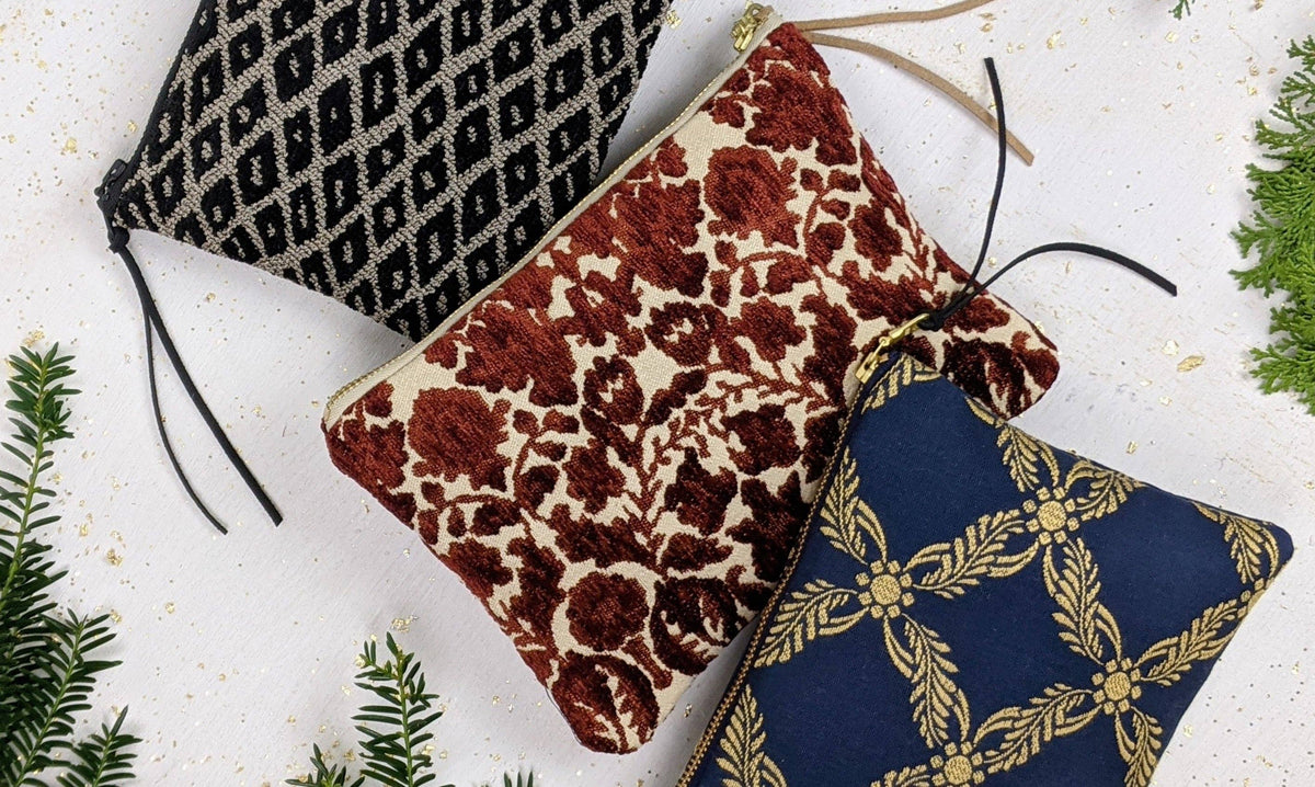 Close-up of three grouped pouches: the black and taupe Black Diamond Needlepoint pouch, a rust floral velvet pouch, and a navy and gold trellis-print pouch