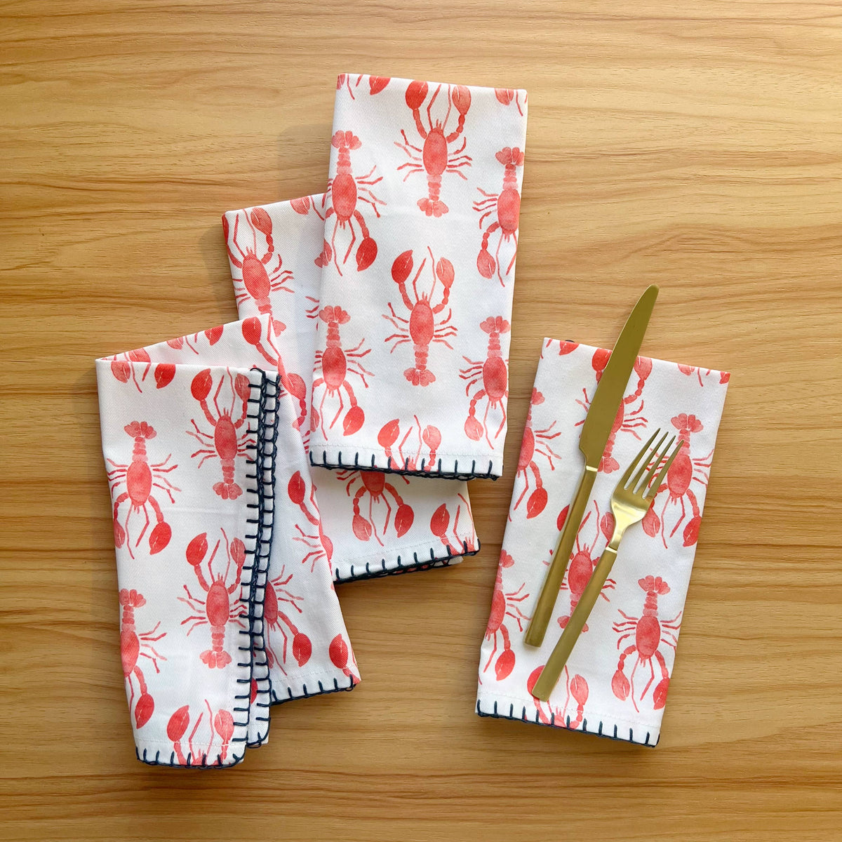 Four lobster napkins on a wood table, one with a gold knife and fork resting on top