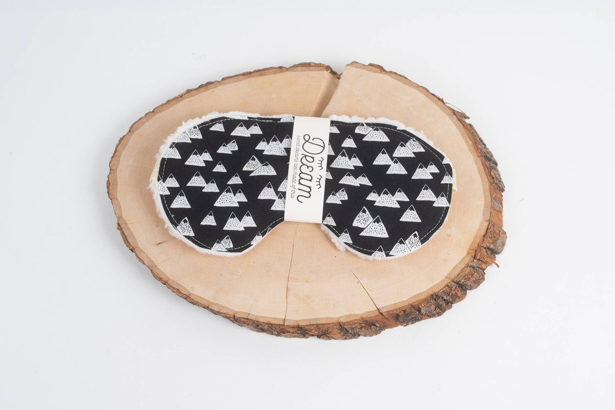 Snow Caps print Dream sleep mask in black with white mountain peaks and a Dream band, on a large natural wood slice