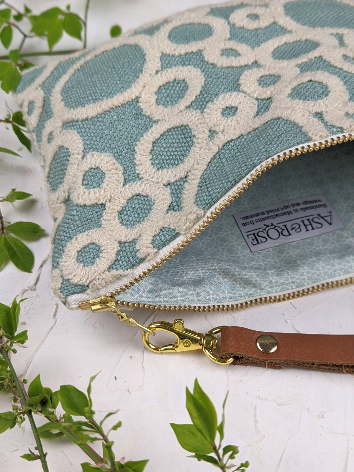 Close-up of open Circle Game wristlet purse showing the Ash & Rose label and zipper pull, seafoam green embroidered exterior