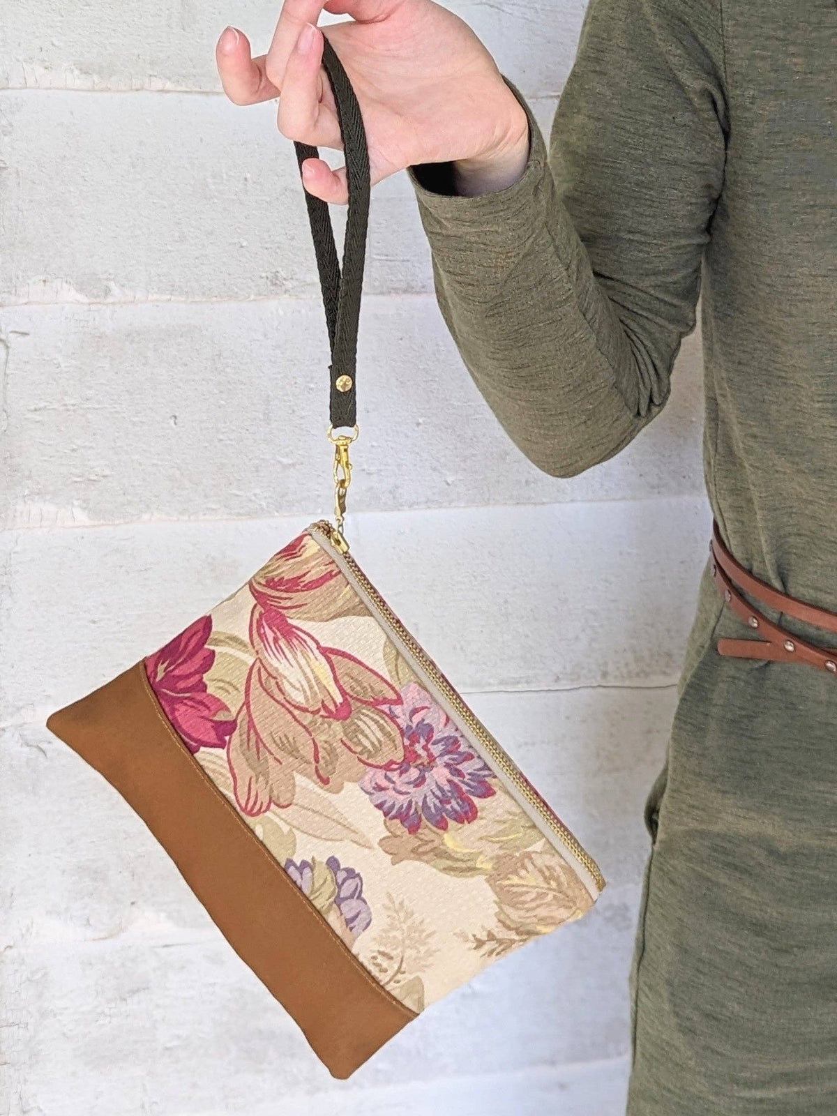 A woman holding a closed Antique Roses wristlet purse against denim jeans, red and pink rose print fabric with tan leather bottom
