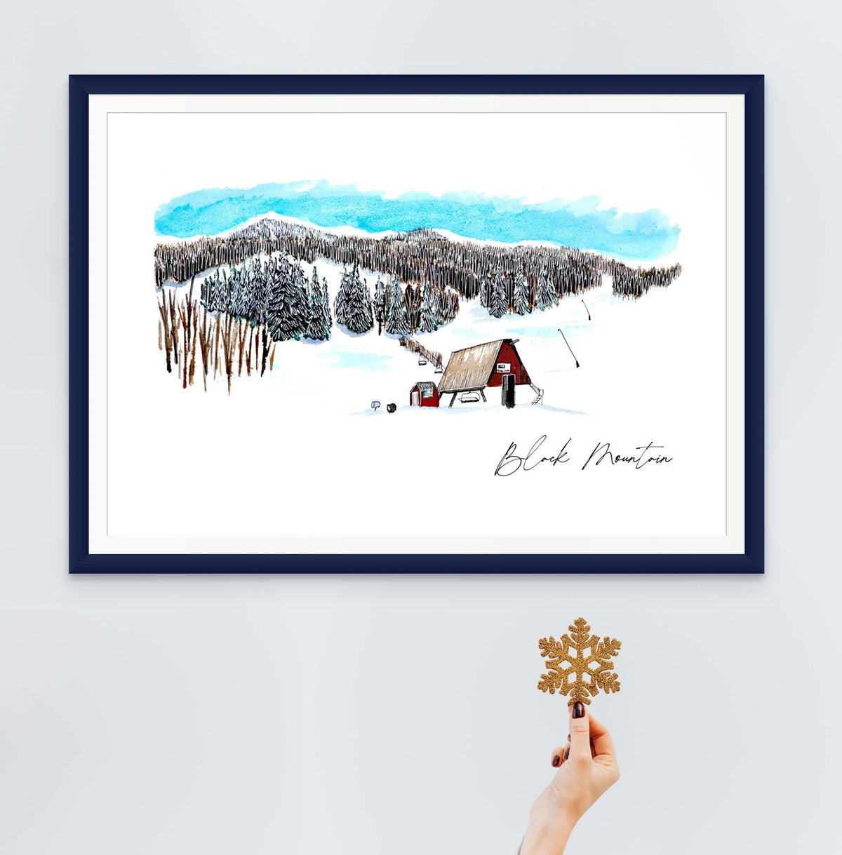 Black Mountain Ski Area print in a navy frame, styled with a hand holding a glitter snowflake ornament