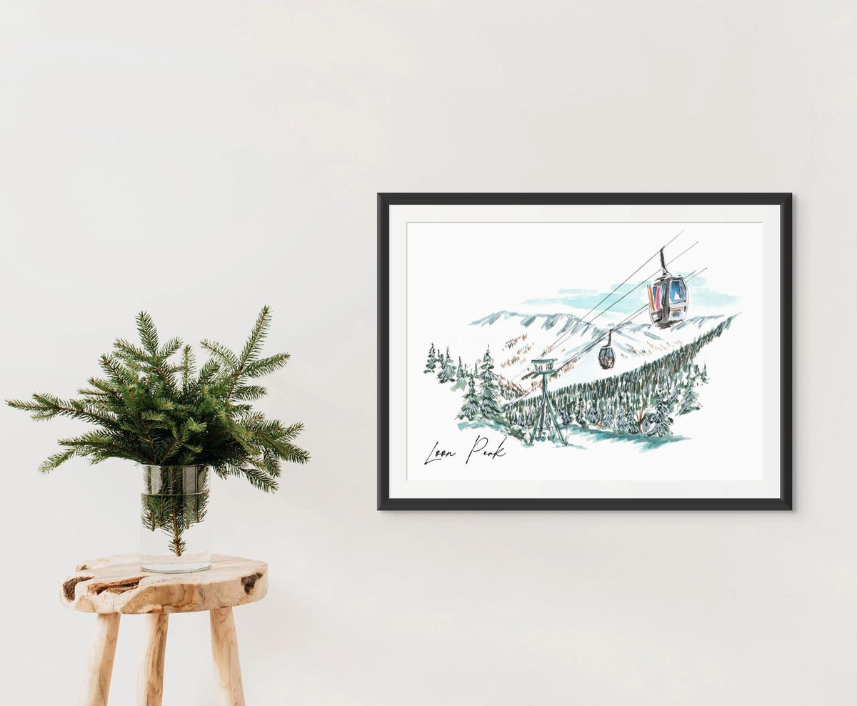 Loon Peak art print in a black frame on a wall, styled with a wooden stool and a vase of pine branches